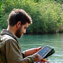 Ecological researcher analyzing fish data on a tablet by a river